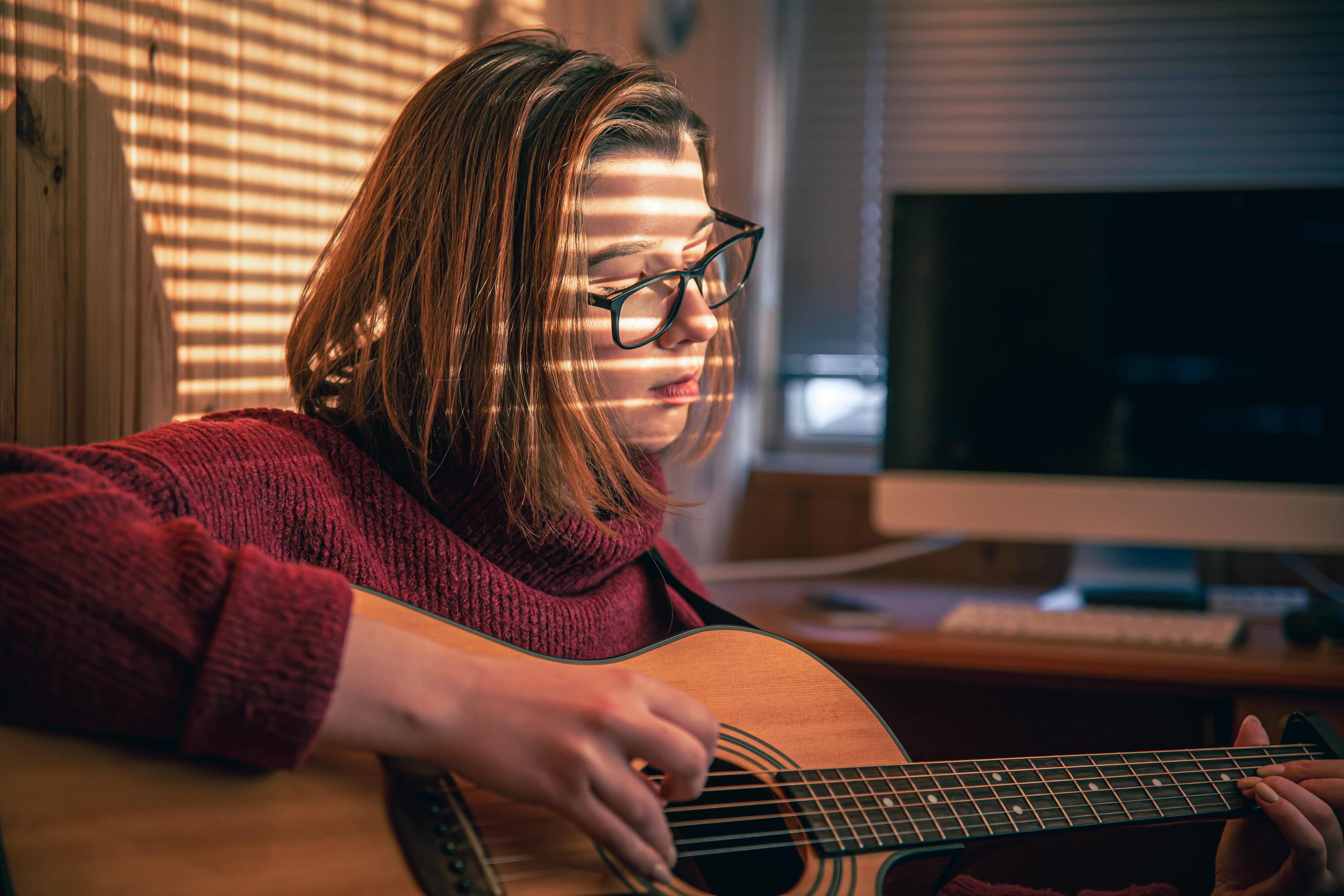 Girl with a guitar in the sunlight through the blinds.