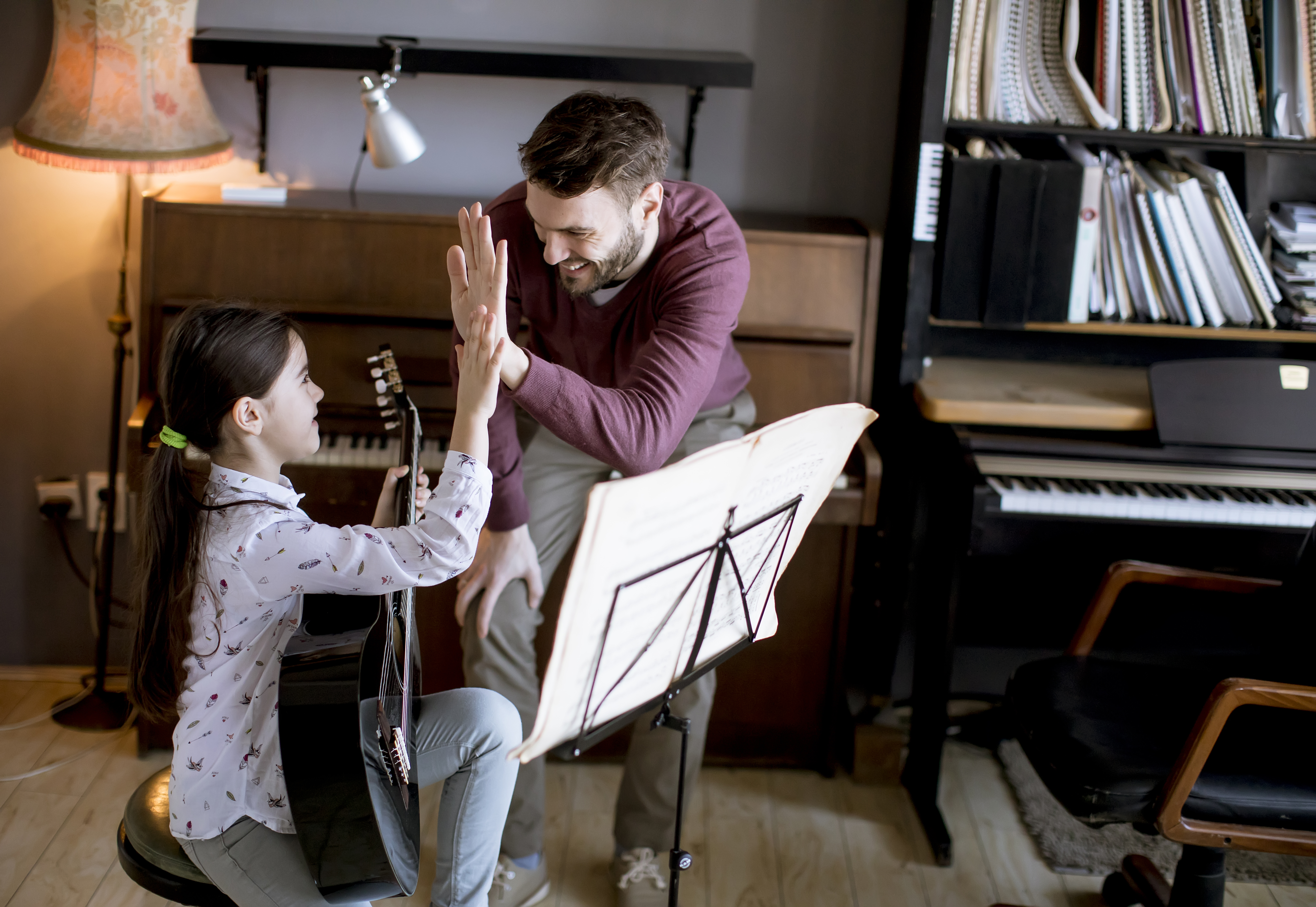 Little girl playing guitar with her music teacher in the rustic apartment